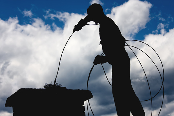 Silhouette of Freehold chimney cleaning being done on roof
by worker using large wire brush